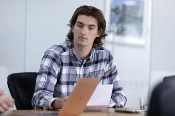 Young Male Sits With Colleague Looking At Laptop